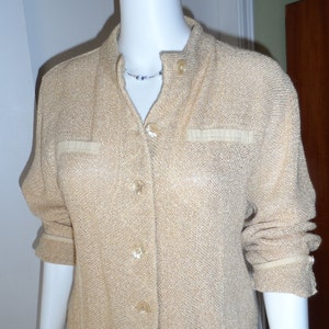 Puede incluir: Un cárdigan beige con botones, mangas largas y tejido de punto texturizado. El cárdigan tiene un cuello mandarín y una sola fila de botones en la parte delantera.