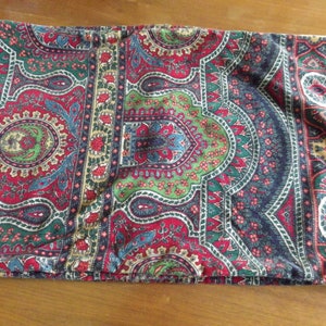 May include: A pillow cover with a paisley pattern in shades of red, green, blue, and gold. The fabric has a textured, almost velvet-like appearance.