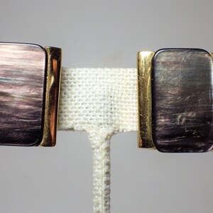 May include: A pair of gold-toned earrings with iridescent black and purple rectangular stones.
