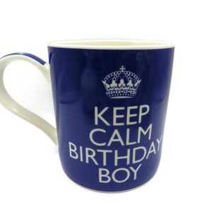 Puede incluir: Taza de cerámica azul con una corona blanca y el texto "Keep Calm Birthday Boy".