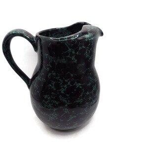 Può includere: Un'anfora in ceramica nera con una glassa verde marmorizzata. L'anfora ha un'ampia apertura e un manico.