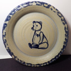 Può includere: Un piatto in ceramica blu e bianco con un disegno di un orso blu. L'orso è seduto e ha un cuore sul petto. Il piatto ha un bordo blu e bianco.