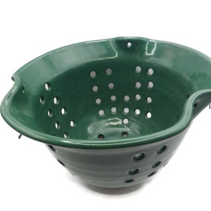 May include: A green ceramic colander with a wavy rim and a hole pattern.