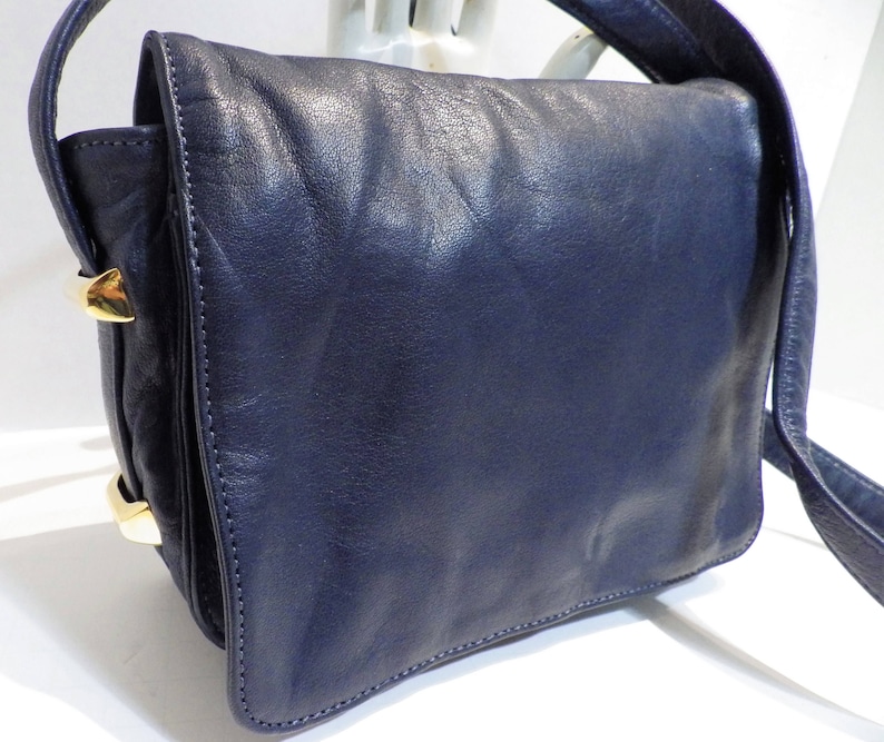 May include: A dark blue leather shoulder bag with gold-toned hardware. The bag has a flap closure and a single strap.