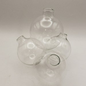 May include: Three clear glass bud vases with round bodies and a small opening at the top. The vases are stacked on top of each other.