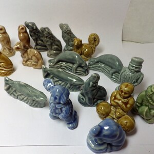 May include: A collection of 17 small ceramic figurines, including animals, people, and a whale. The figurines are painted in various shades of blue, green, brown, and gray.