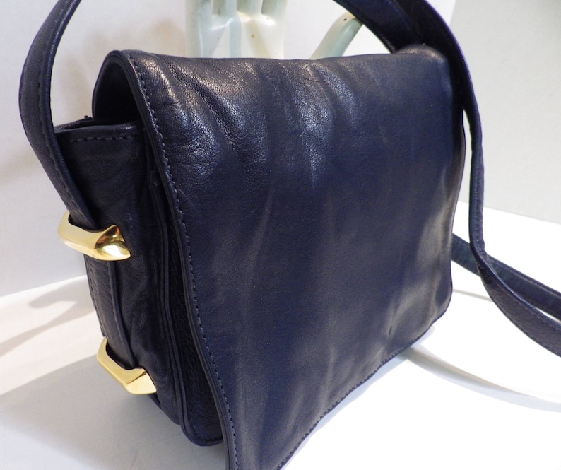 May include: A dark blue leather shoulder bag with a gold clasp and a long strap.