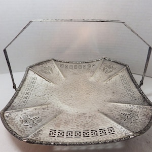 May include: A silver serving tray with a hammered finish and intricate cut-out designs. The tray has a handle and is ideal for serving snacks or appetizers.