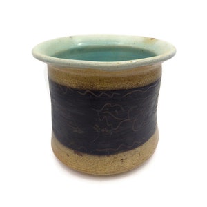 May include: A brown and black ceramic mug with a light blue glaze inside. The mug has a wavy design around the middle and a textured surface.