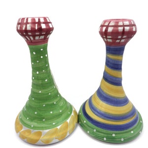 May include: Two ceramic candle holders with a green and yellow design and a blue and yellow design. The top of each holder is red and white checkered.