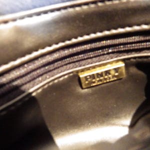 May include: Close-up of the inside of a black leather purse with a gold metal label that reads "Pinky London".