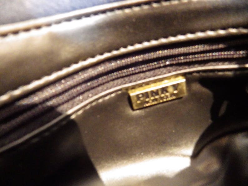 May include: Close-up of the inside of a black leather purse with a gold metal label that reads "Pinky London".