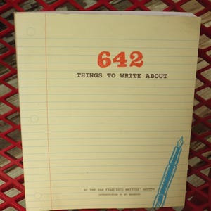 May include: A notepad with a cream-colored paper and blue horizontal lines. The cover features the title "642 THINGS TO WRITE ABOUT" in red and black text, along with a blue pen illustration. The notepad is designed to inspire creative writing.