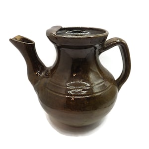 Può includere: Una teiera in ceramica marrone con corpo arrotondato e manico. La teiera ha un beccuccio e un coperchio.