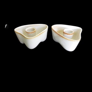 May include: Two white ceramic candle holders with a brown glaze around the top edge. Each holder has a round, recessed area in the center for a candle.