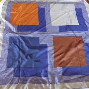 May include: A square silk scarf with a geometric pattern of orange, brown, blue, and gray squares on a white background. The scarf has a silver border and the word "Walter" printed in the bottom right corner.