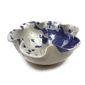 May include: A white ceramic bowl with a blue and white splatter design. The bowl has a ruffled edge and a center hole.