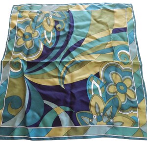 May include: Square silk scarf with a floral and abstract design. The scarf features a color palette of teal, navy, olive green, and cream. The design includes stylized flowers and swirling patterns, framed by a white border.