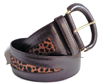 May include: A brown leather belt with a leopard print design. The belt has a gold buckle and is approximately 7.5 cm wide.