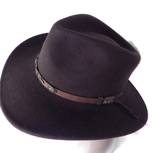 May include: A brown felt fedora hat with a brown leather band and metal accents. The hat has a wide brim and a tall crown.
