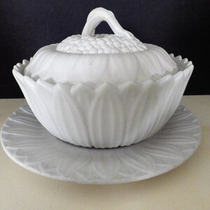 May include: White milk glass butter dish with a lid shaped like a flower. The dish has a scalloped edge and the lid has a knob in the center.