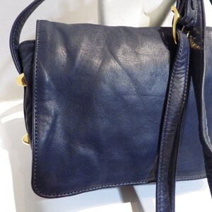 May include: A dark blue leather shoulder bag with a gold buckle and a long strap.
