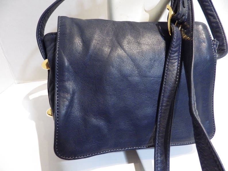 May include: A dark blue leather shoulder bag with a gold buckle and a long strap.