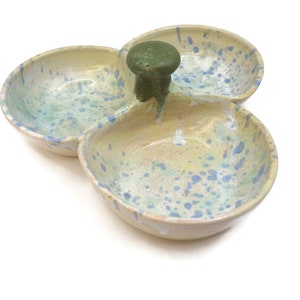 May include: A three-section ceramic serving dish with a green knob handle. The dish is decorated with a light yellow glaze and blue and green speckles.