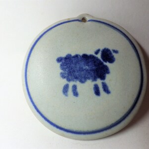 May include: A white ceramic ornament with a blue outline and a blue silhouette of a sheep.