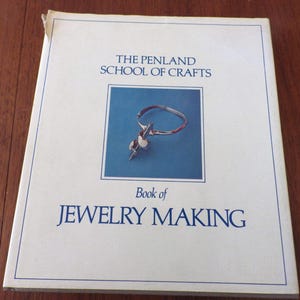 May include: A white book with the title "The Penland School of Crafts Book of Jewelry Making". The cover features a photo of a silver necklace with a blue background.