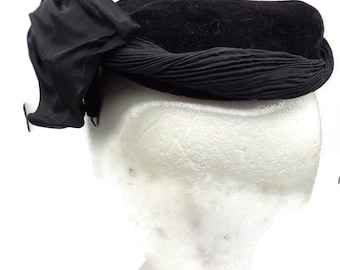 Puede incluir: Un sombrero de terciopelo negro con un gran lazo negro en un lado.
