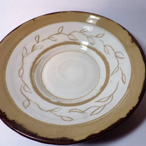 May include: A white ceramic plate with a brown rim and a white leaf design. The plate has a slightly raised center.