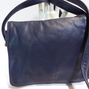 May include: A dark blue leather shoulder bag with a flap closure and a single strap. The bag has a worn look and is made of a soft, supple leather.