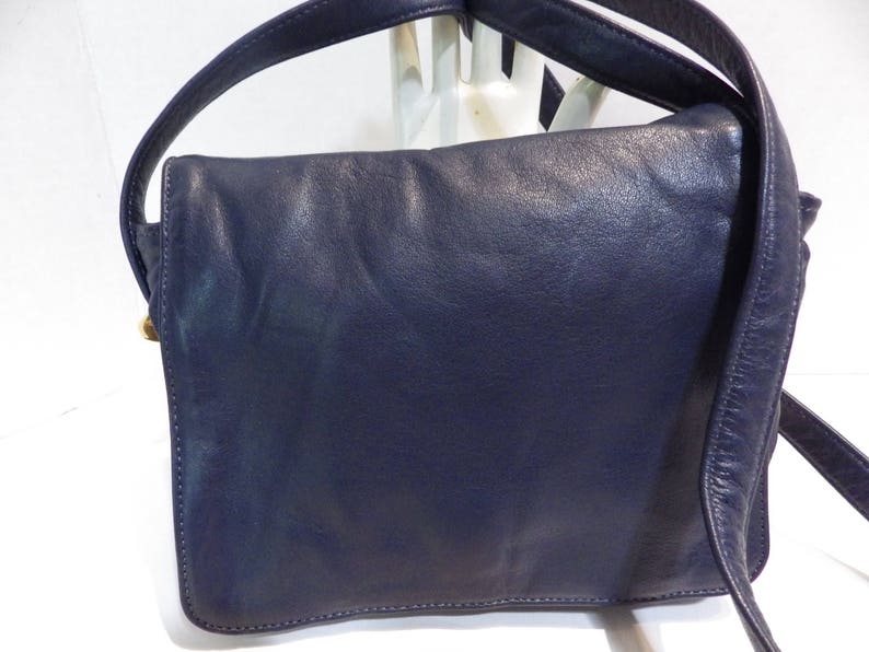 May include: A dark blue leather shoulder bag with a flap closure and a single strap. The bag has a worn look and is made of a soft, supple leather.