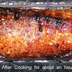 Puede incluir: Un lomo de cerdo asado en un asador, brillando con un glaseado marr&oacute;n y granos de pimienta. El cerdo se cocina en una parrilla negra con una rejilla de metal. "Despu&eacute;s de cocinar durante aproximadamente una hora" est&aacute; escrito debajo del cerdo.