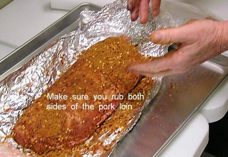 Puede incluir: Primer plano de un lomo de cerdo cubierto con una mezcla de especias y envuelto en papel de aluminio. El texto "Make sure you rub both sides of the pork loin" es visible en la imagen.