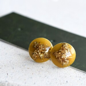 May include: A pair of gold and yellow round stud earrings with gold flecks embedded in the resin.