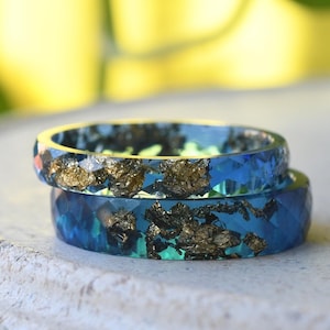 May include: Two blue resin rings with gold flakes embedded in the resin. The rings are stacked on top of each other.