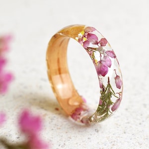 May include: A clear resin ring with a wood band and embedded pink and green flowers.