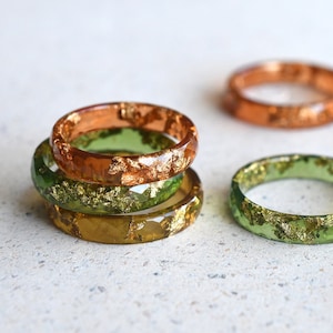 May include: A set of four resin rings with gold leaf accents. The rings are in shades of green and orange.