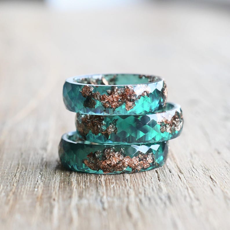 Three handmade resin rings including jade, aquamarine, and pink flower styles arranged in a group on fabric.