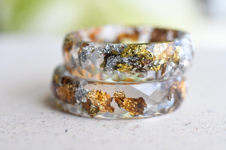K&ouml;nnte beinhalten: Zwei transparente Harzringe mit eingebetteten Gold- und Silberflocken. Die Ringe sind &uuml;bereinander gestapelt.