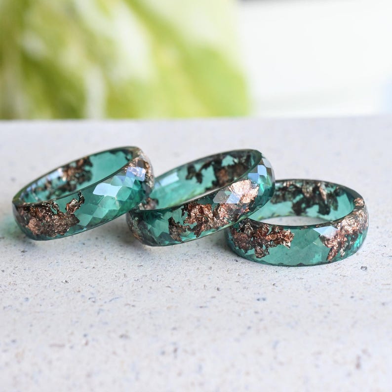 Macro view of metallic rose gold leaf detail set inside translucent jade green resin ring.