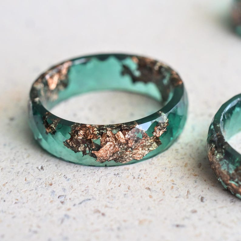 Jade resin ring with rose gold flakes displayed on a clean white background, showing smooth surface and light reflection.