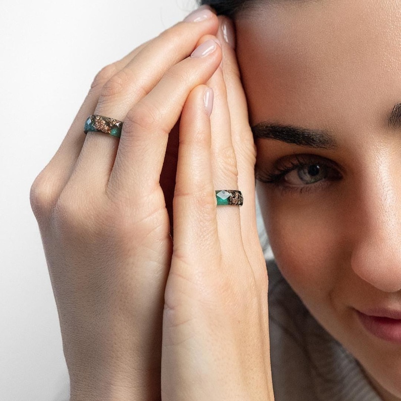 May include: Two rings with a turquoise and brown speckled design are displayed on fingers. The rings have a band of brown speckled material with a turquoise center. The rings are on a person's fingers, with the person's face in the background.