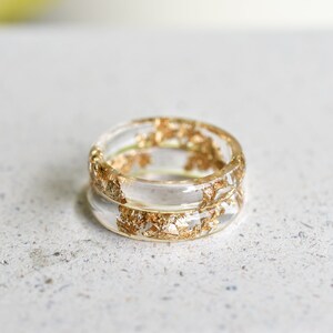 May include: A clear resin ring with gold leaf embedded in the resin. The ring is double-banded and has a simple, elegant design.