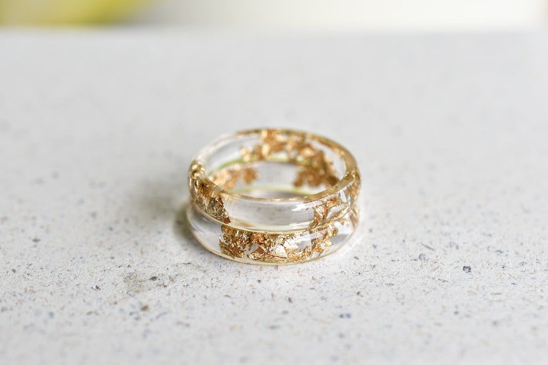 May include: A clear resin ring with gold leaf embedded in the resin. The ring is double-banded and has a simple, elegant design.