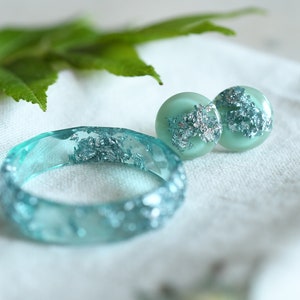 Puede incluir: Un conjunto de joyas de resina turquesa con escamas plateadas. El conjunto incluye una pulsera y un par de pendientes.