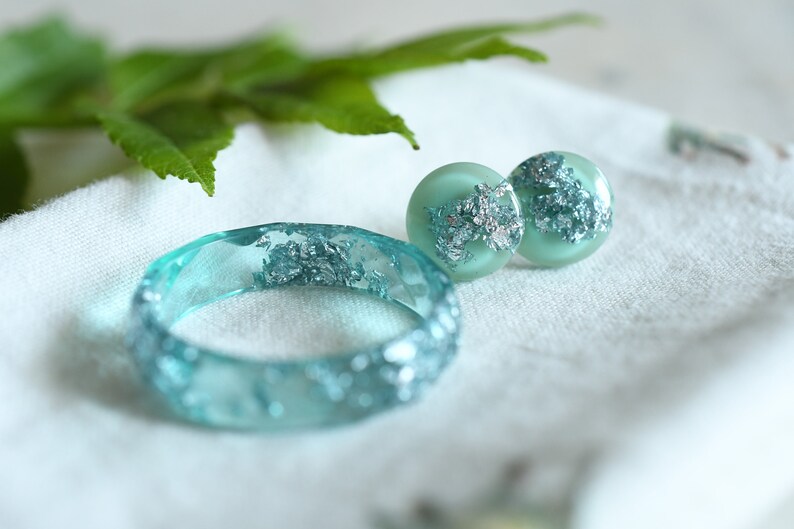 Puede incluir: Un conjunto de joyas de resina turquesa con escamas plateadas. El conjunto incluye una pulsera y un par de pendientes.