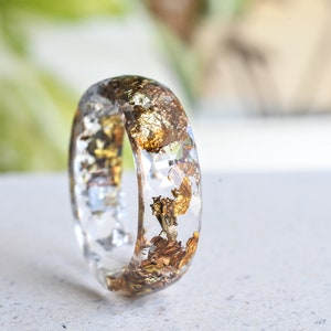 K&ouml;nnte beinhalten: Ein klarer Harzring mit eingebettetem Blattgold. Der Ring ist dick und hat eine abgerundete Form.